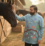 Man in a linen kurta with hand-painted Bhil motif gently touching a horse, showing fabric texture, movement, and surface interaction in natural light.