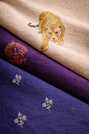 Close-up of linen fabric showing painted and embroidered motifs sitting on the surface, highlighting texture, fibre structure, and material behaviour.