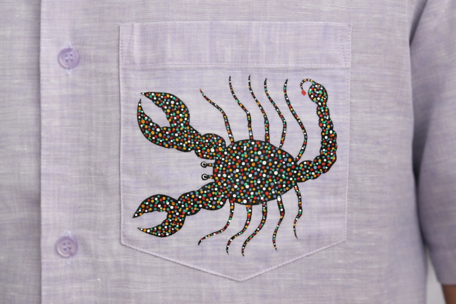 Close-up of hand-painted Bhil scorpion artwork on linen shirt pocket showing intricate dot work.