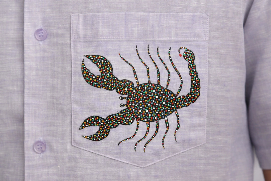 Close-up of hand-painted Bhil scorpion artwork on linen shirt pocket showing intricate dot work.