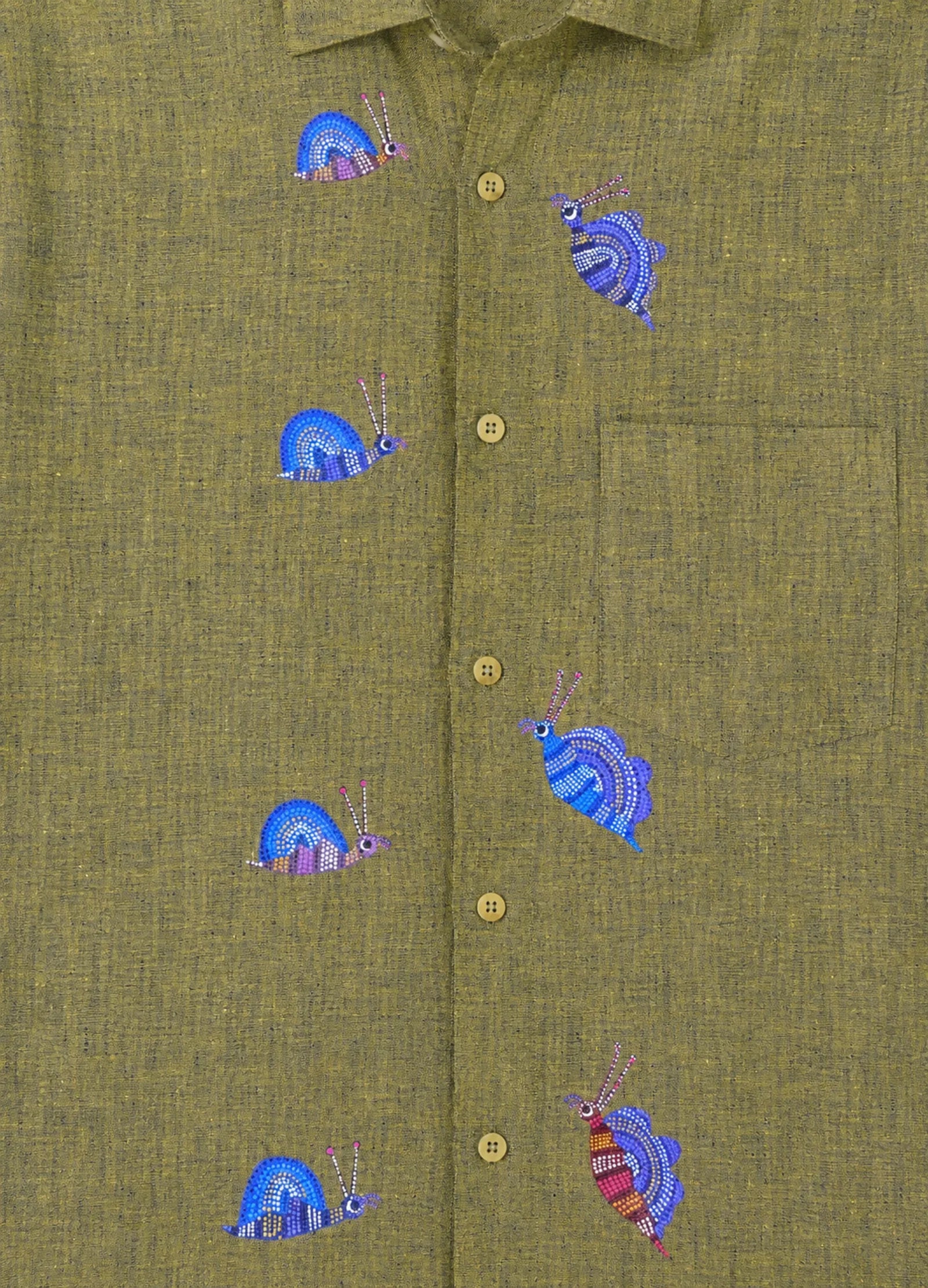 Bhil hand-painted linen shirt featuring seven snail artworks arranged across the front panel, photographed at the entrance of a limestone cave during an early morning exploration.