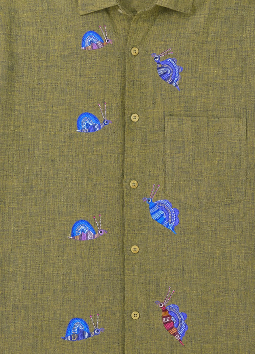Bhil hand-painted linen shirt featuring seven snail artworks arranged across the front panel, photographed at the entrance of a limestone cave during an early morning exploration.