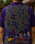 Hand-painted Bhil linen shirt featuring a Mahua tree artwork across the back with male and female figures alongside a child collecting blossoms, accompanied by birds, grazing deer, and fruit-bearing branches, shown in a rear close-up view within a rustic outdoor setting.