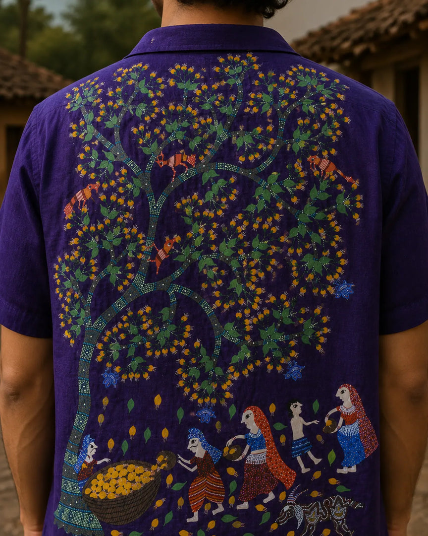 Hand-painted Bhil linen shirt featuring a Mahua tree artwork across the back with male and female figures alongside a child collecting blossoms, accompanied by birds, grazing deer, and fruit-bearing branches, shown in a rear close-up view within a rustic outdoor setting.