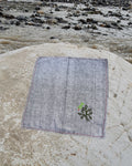 Hand-embroidered Bihar Sujani khadi handkerchief with a bird perched on a leafy tree artwork, photographed on a weathered river stone.