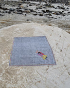 Hand-embroidered Bihar Sujani khadi handkerchief featuring a woman carrying a basket of food artwork, photographed on a weathered river stone.