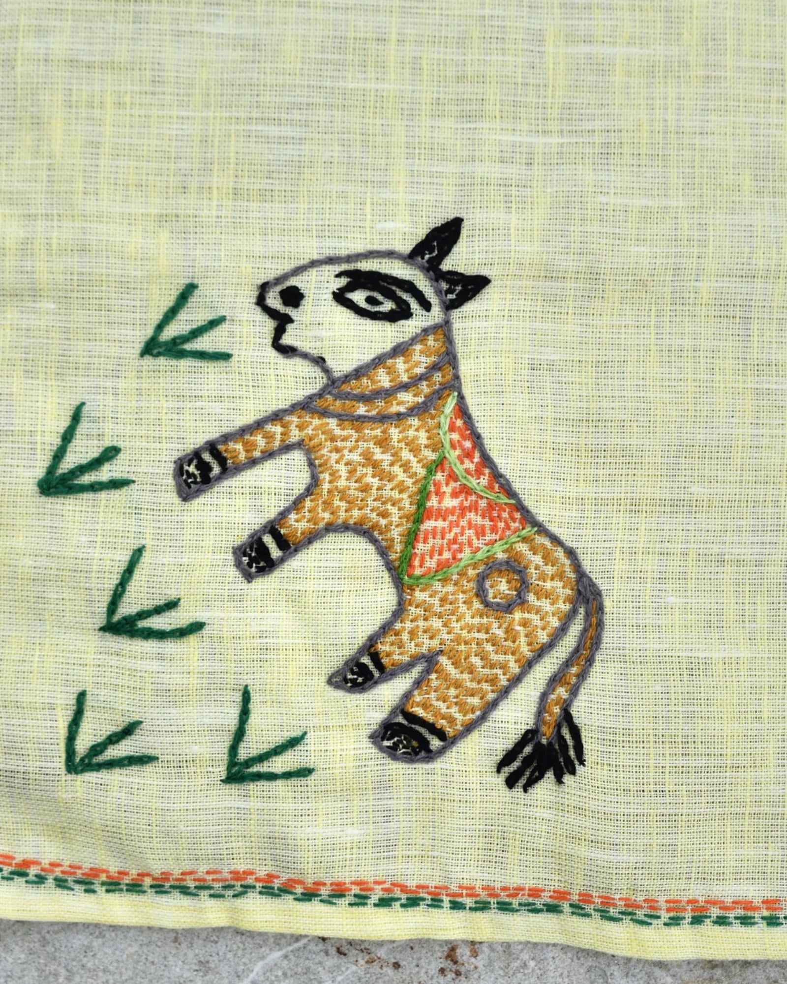 Close-up of artwork depicting a hand-embroidered cow grazing on grass on a Bihar Sujani linen handkerchief.