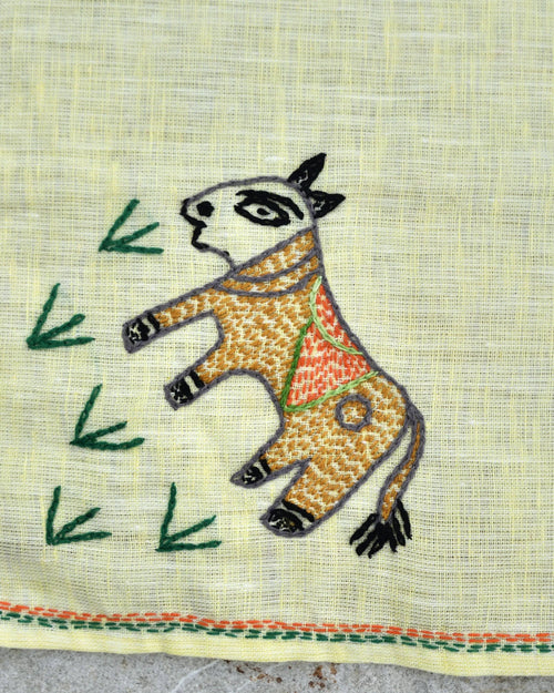 Close-up of artwork depicting a hand-embroidered cow grazing on grass on a Bihar Sujani linen handkerchief.