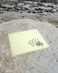 Bihar Sujani hand-embroidered linen handkerchief featuring a flowering tree artwork, photographed on a weathered river stone in a natural riverside setting.