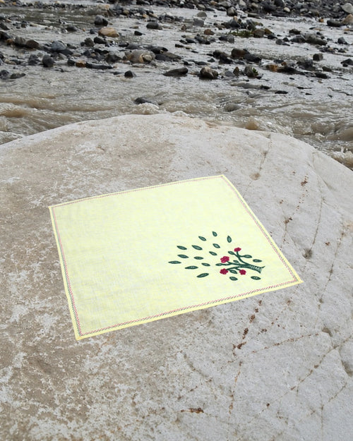 Bihar Sujani hand-embroidered linen handkerchief featuring a flowering tree artwork, photographed on a weathered river stone in a natural riverside setting.