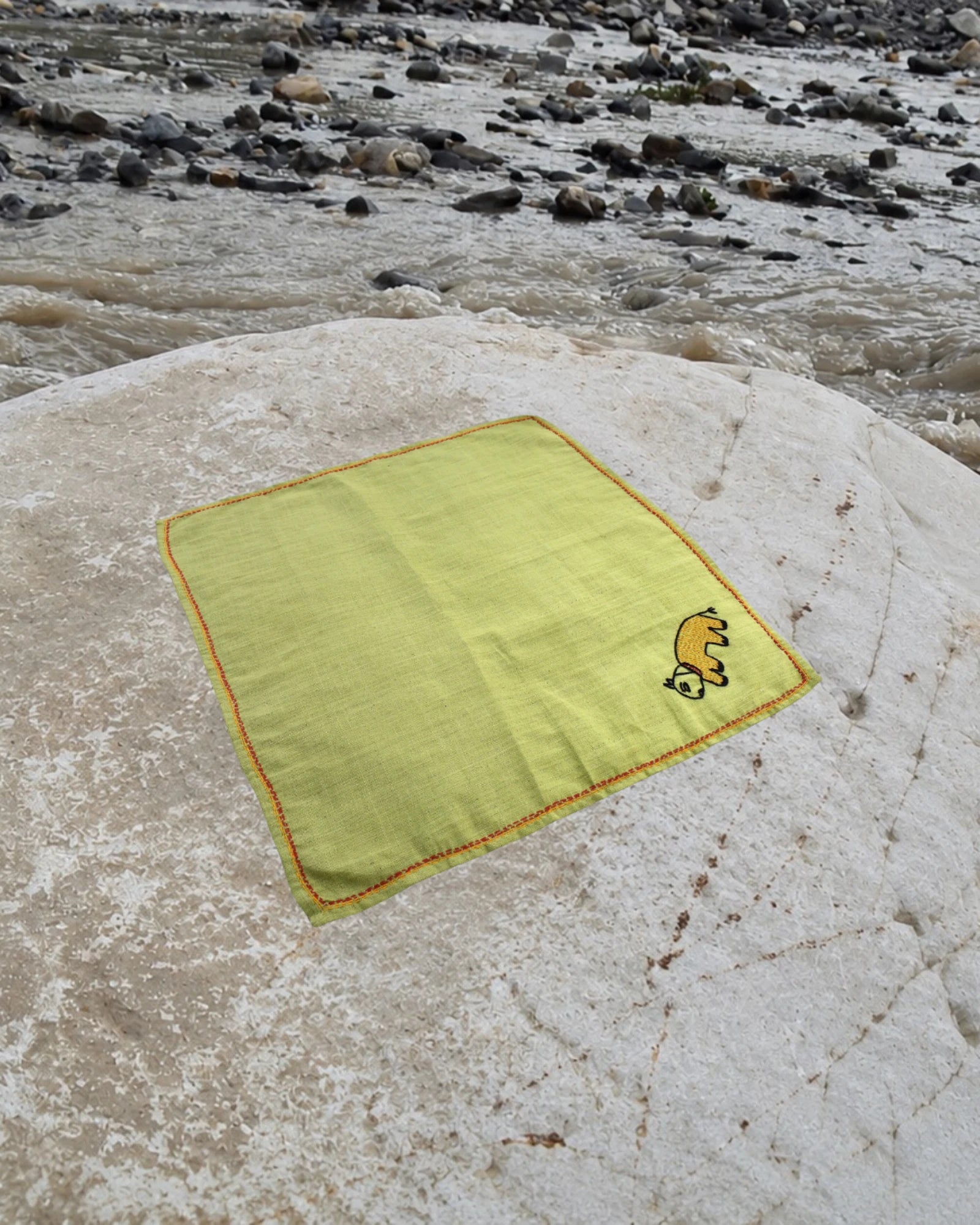 Hand-embroidered Bihar Sujani khadi handkerchief featuring a pet animal artwork, photographed on a weathered river stone.