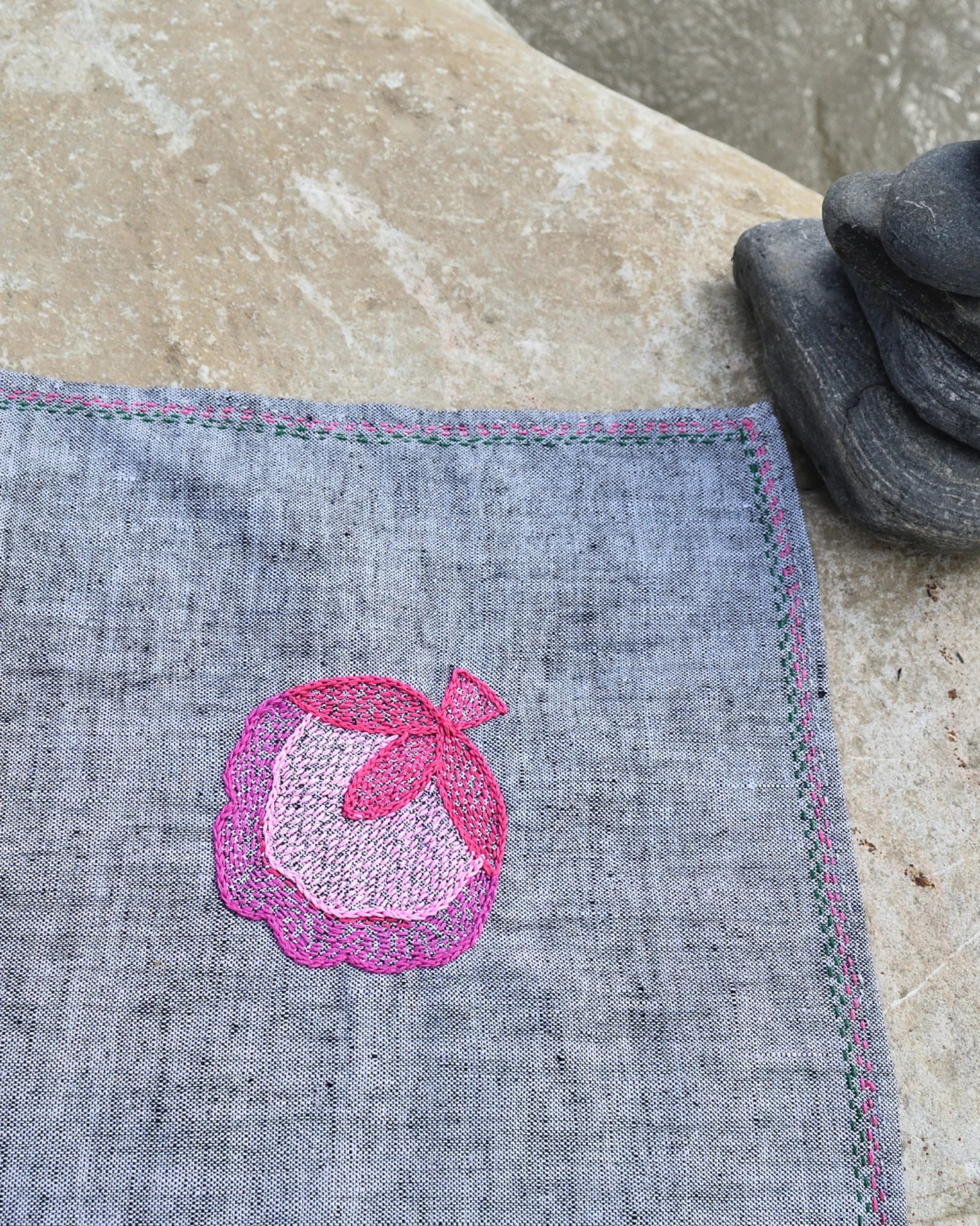 Close-up of hand-embroidered pink flower blossom artwork on a khadi cotton Bihar Sujani handkerchief, highlighting the floral embroidery and hand-finished border.