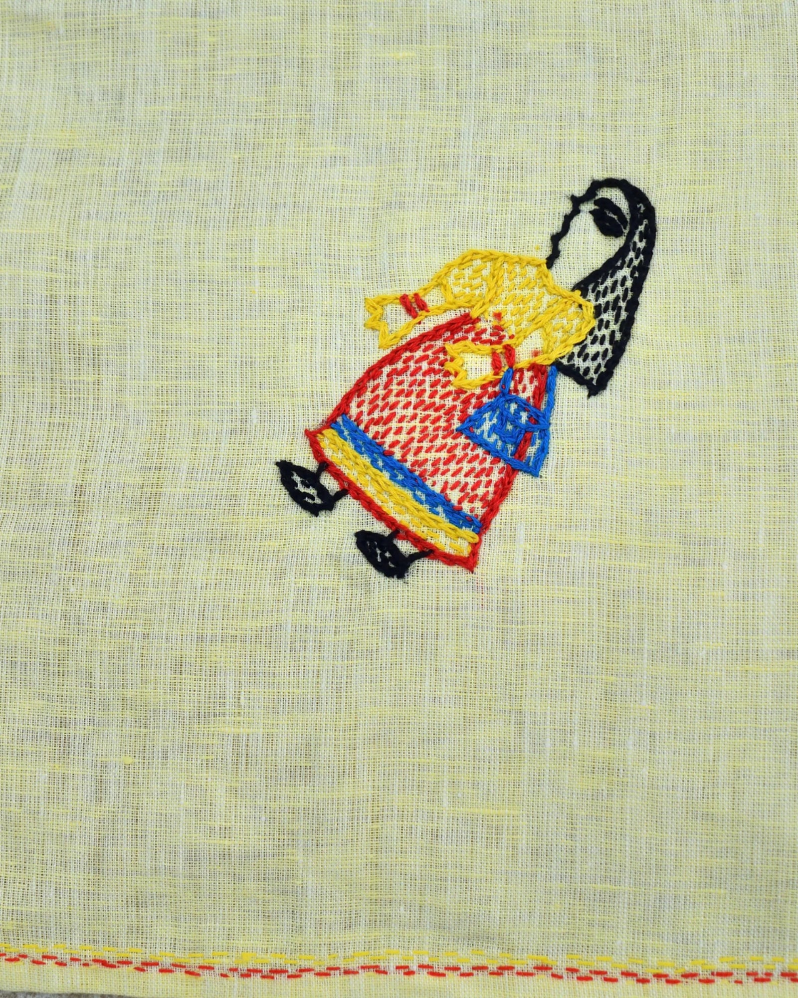 Close-up of artwork depicting a woman carrying a shopping bag on a Bihar Sujani hand-embroidered linen handkerchief.