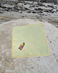Hand-embroidered Bihar Sujani linen handkerchief featuring artwork of a woman carrying a shopping bag, photographed on a weathered river stone.