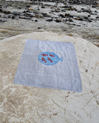 Hand-embroidered Bihar Sujani khadi handkerchief featuring a large blue fish artwork enclosing four red fish artworks, photographed on a weathered river stone.