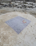 Hand-embroidered Bihar Sujani khadi handkerchief featuring a flowering branch artwork, photographed on a weathered river stone.