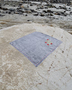 Hand-embroidered Bihar Sujani khadi handkerchief featuring a flowering branch artwork, photographed on a weathered river stone.