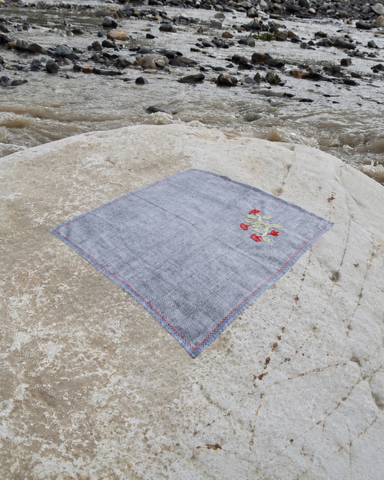 Hand-embroidered Bihar Sujani khadi handkerchief featuring a flowering branch artwork, photographed on a weathered river stone.