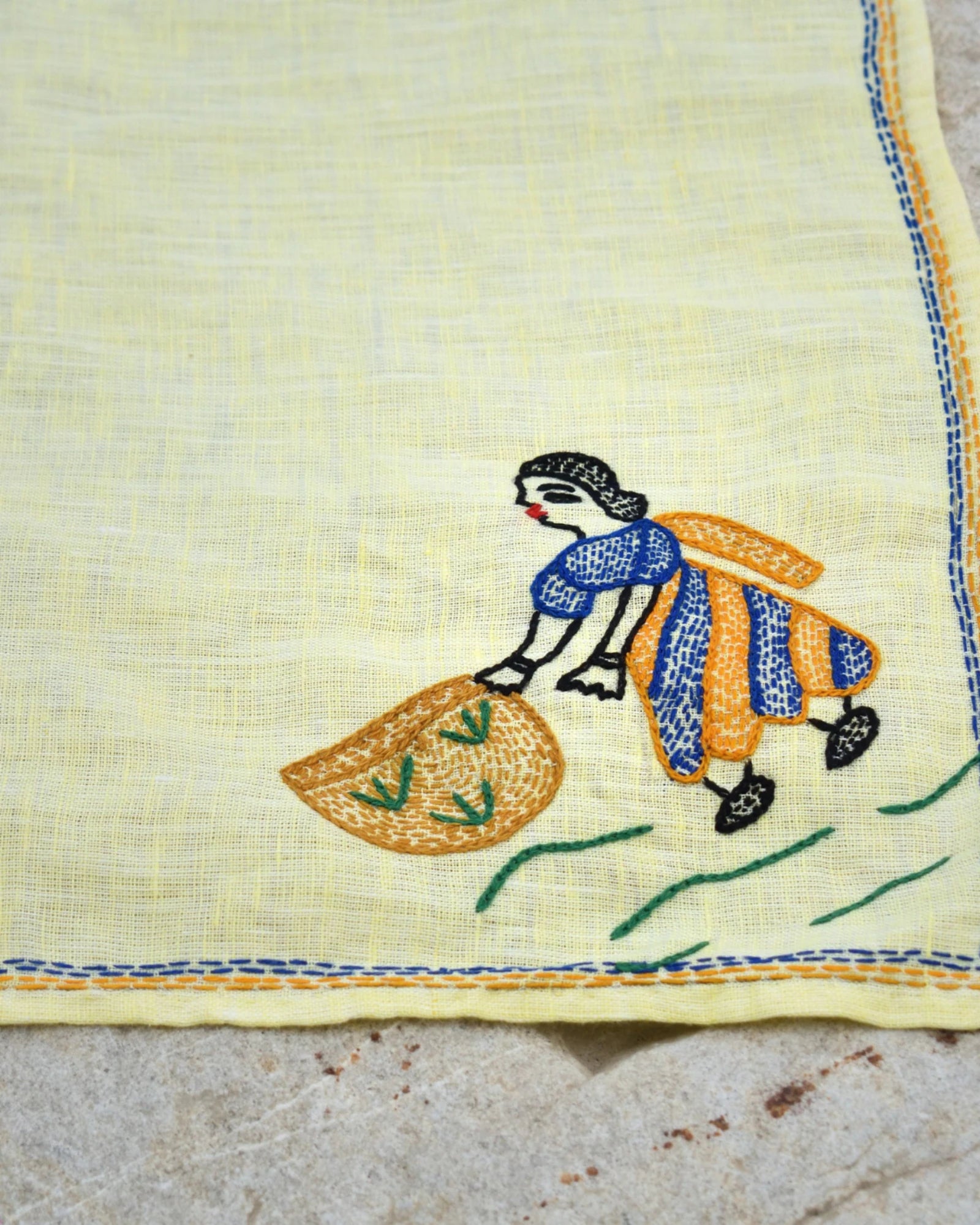 Close-up of a Bihar Sujani hand-embroidered linen handkerchief featuring artwork of a woman gathering the harvest.