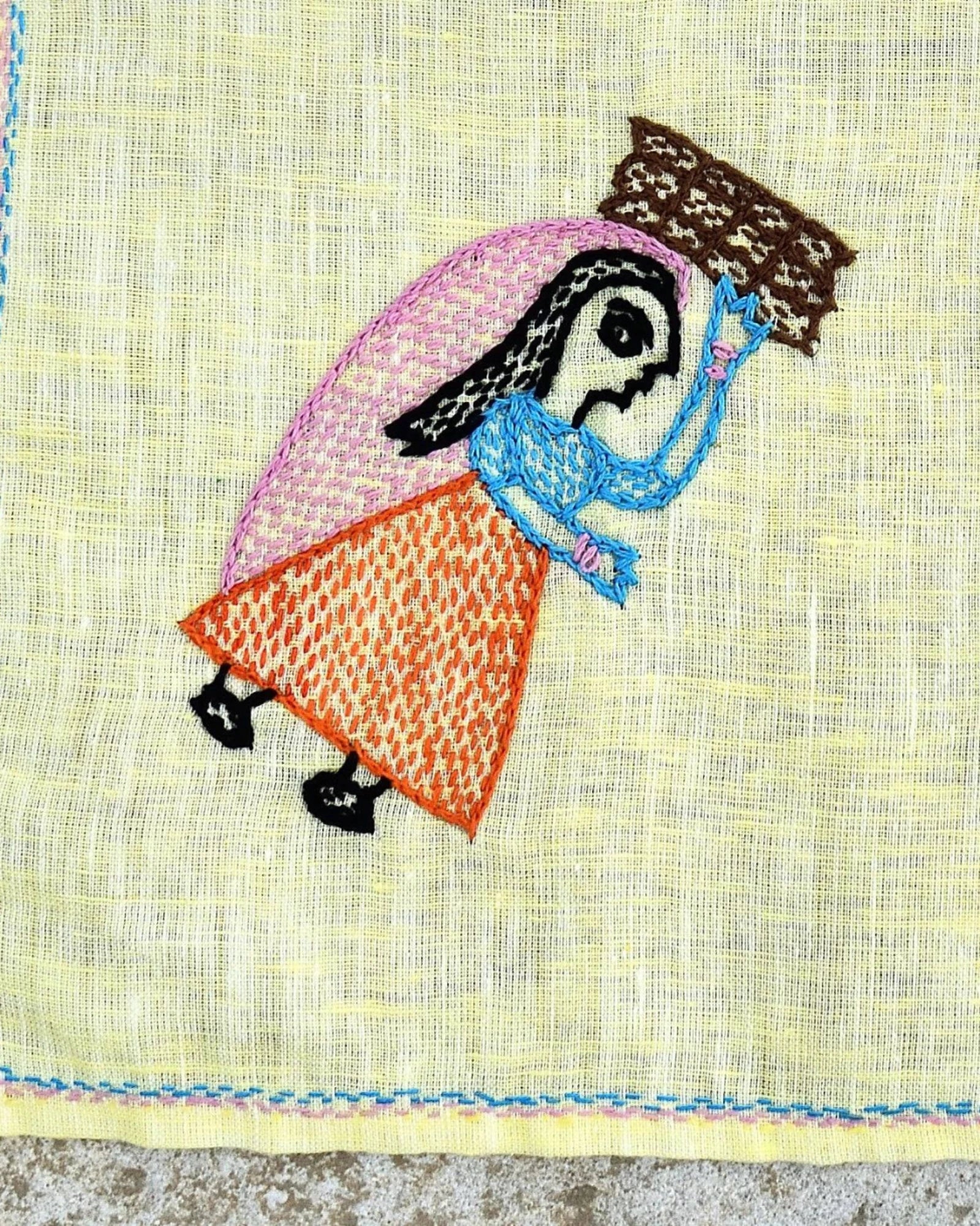 Close-up of artwork depicting a woman carrying a bundle of firewood on a Bihar Sujani hand-embroidered linen handkerchief.