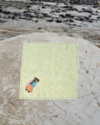 Hand-embroidered Bihar Sujani linen handkerchief featuring artwork of a woman carrying a bundle of firewood, photographed on a weathered river stone.