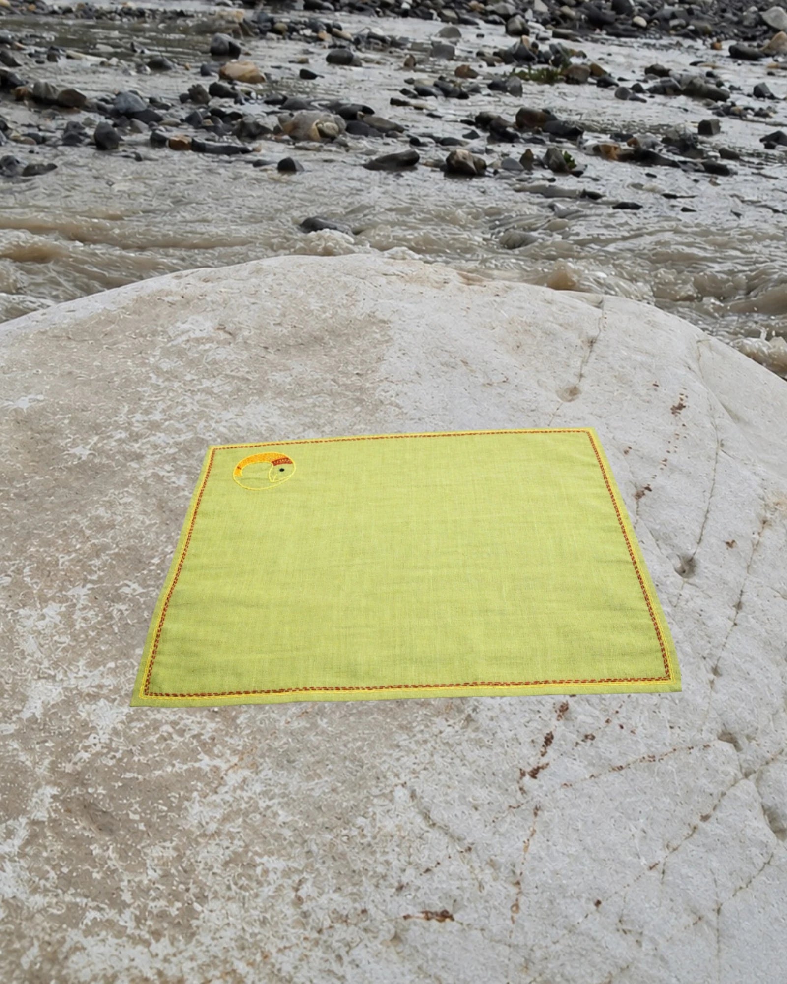 Hand-embroidered Bihar Sujani khadi handkerchief featuring a Yin Yang fish artwork, photographed on a weathered river stone.