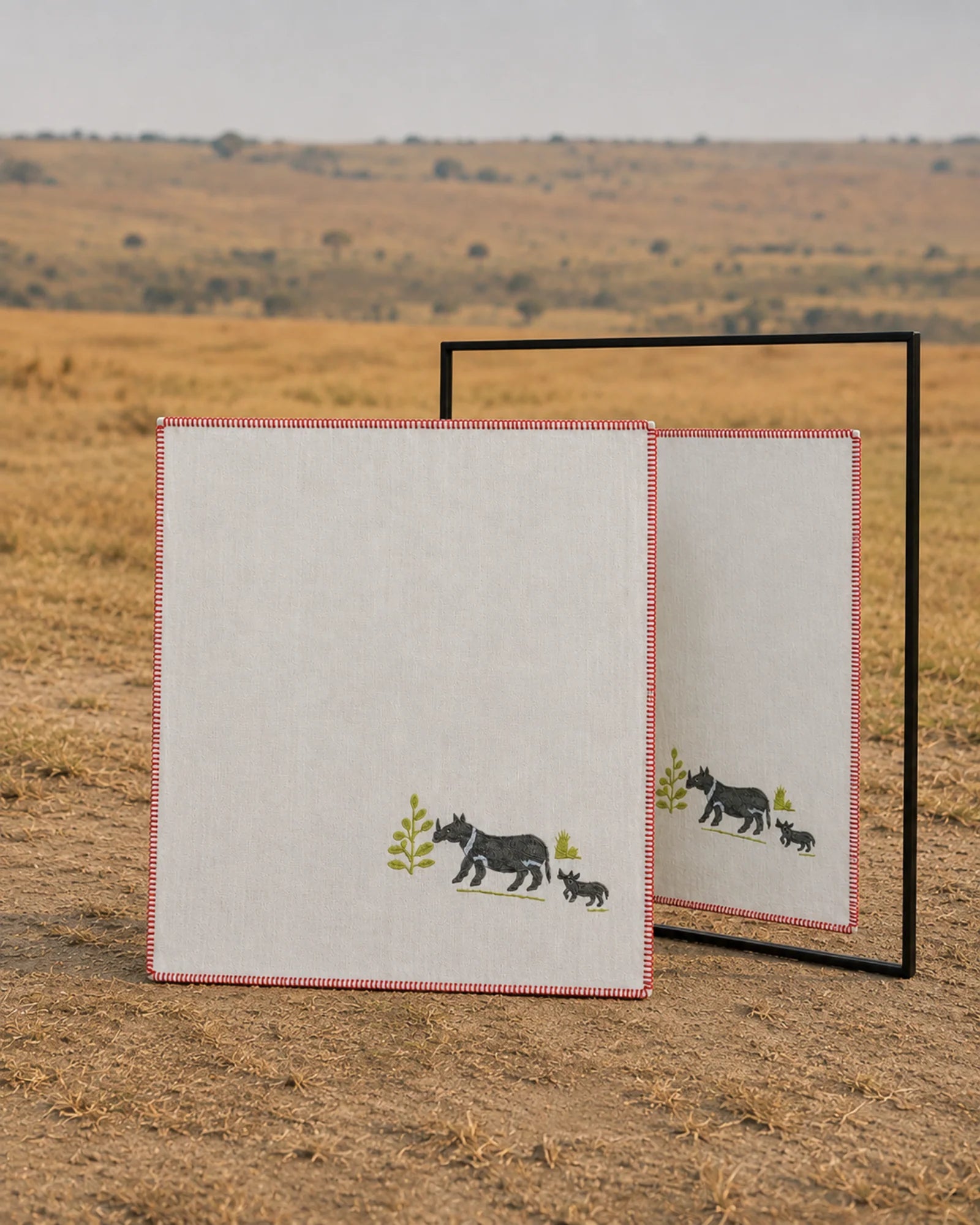 Chamba Rumal from the Jungle collection in handwoven khadi cotton, featuring a hand-embroidered rhinoceros and calf in the lower-left corner, shown with a mirror revealing the identical do-rukha embroidery on both sides.