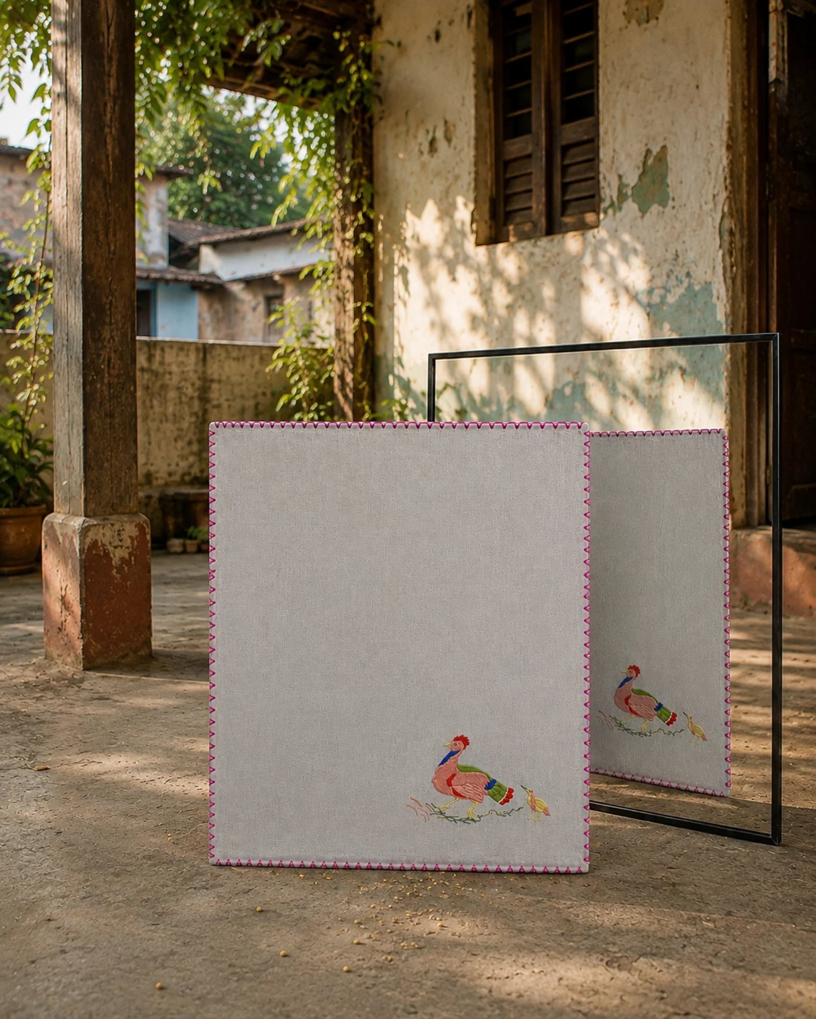 Chamba Rumal from the Jungle Collection crafted in handwoven khadi cotton, featuring a hand embroidered rooster and chick scene in the lower-left corner, hand hemmed and displayed before a mirror revealing identical embroidery on both sides through the traditional do-rukha technique.