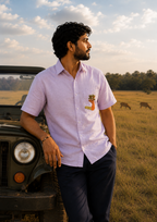 Gond hand-painted linen shirt featuring a deer motif whose antlers transform into branching trees, positioned on the front pocket and photographed beside a vintage jeep in a grassland landscape at golden hour.