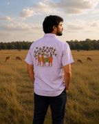 Gond hand-painted linen shirt featuring deer and tree forms across the back panel, observed within open grasslands beside grazing deer in soft natural light.