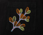 Gond hand-painted linen shirt pocket close-up featuring a hand-painted branching botanical form composed of layered leaf structures and extending tree-like stems, constructed through patterned linear detailing on a structured chest pocket.