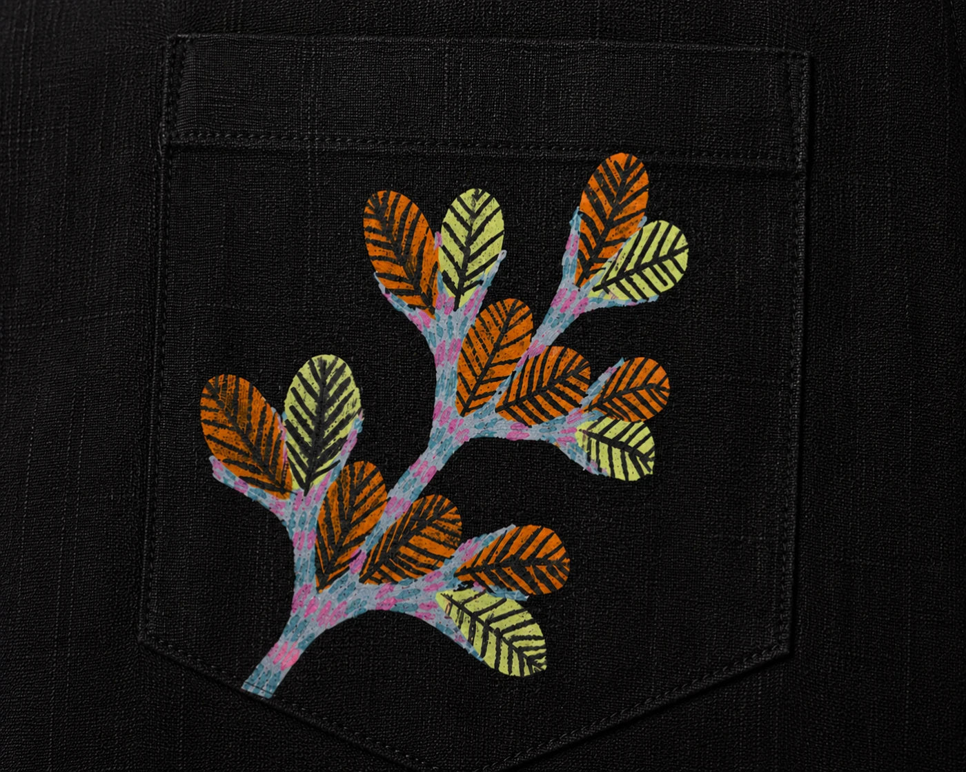Gond hand-painted linen shirt pocket close-up featuring a hand-painted branching botanical form composed of layered leaf structures and extending tree-like stems, constructed through patterned linear detailing on a structured chest pocket.