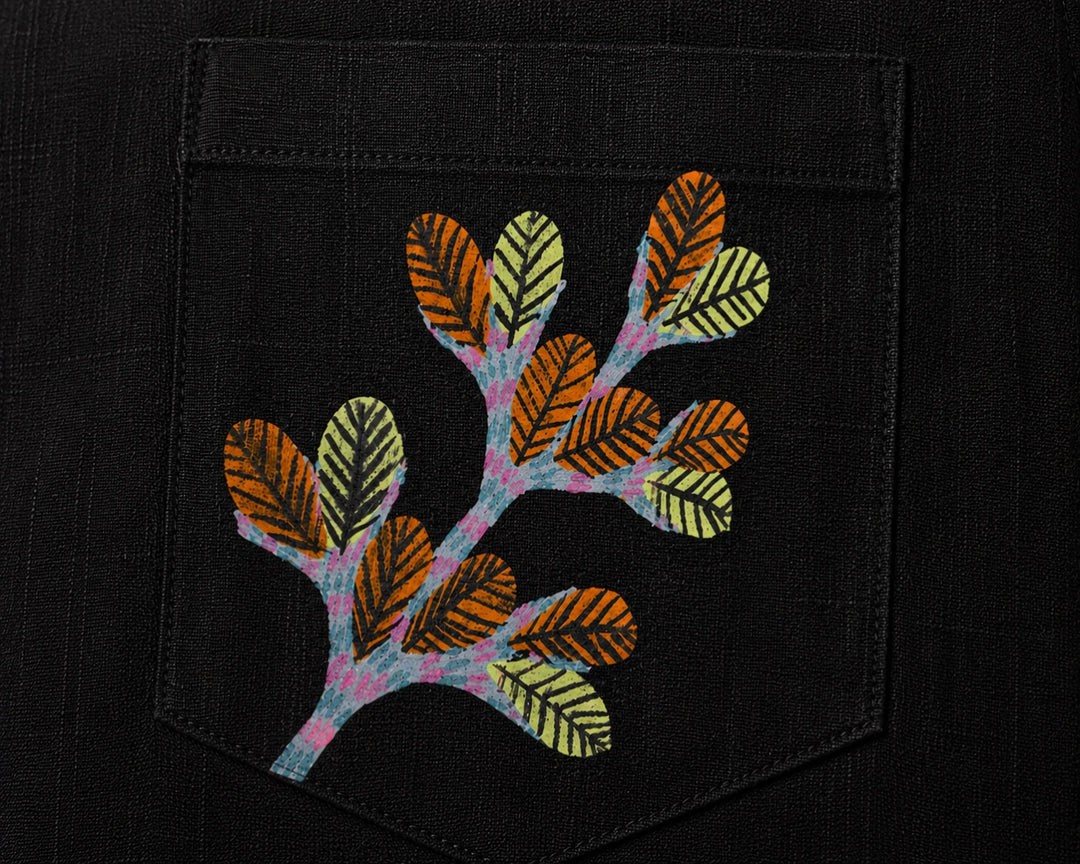 Gond hand-painted linen shirt pocket close-up featuring a hand-painted branching botanical form composed of layered leaf structures and extending tree-like stems, constructed through patterned linear detailing on a structured chest pocket.