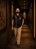 Load image into Gallery viewer, Gond hand-painted linen shirt featuring branching botanical forms along the front placket and chest pocket, observed in an archival corridor setting with softly blurred folk art panels and warm presentation lighting.