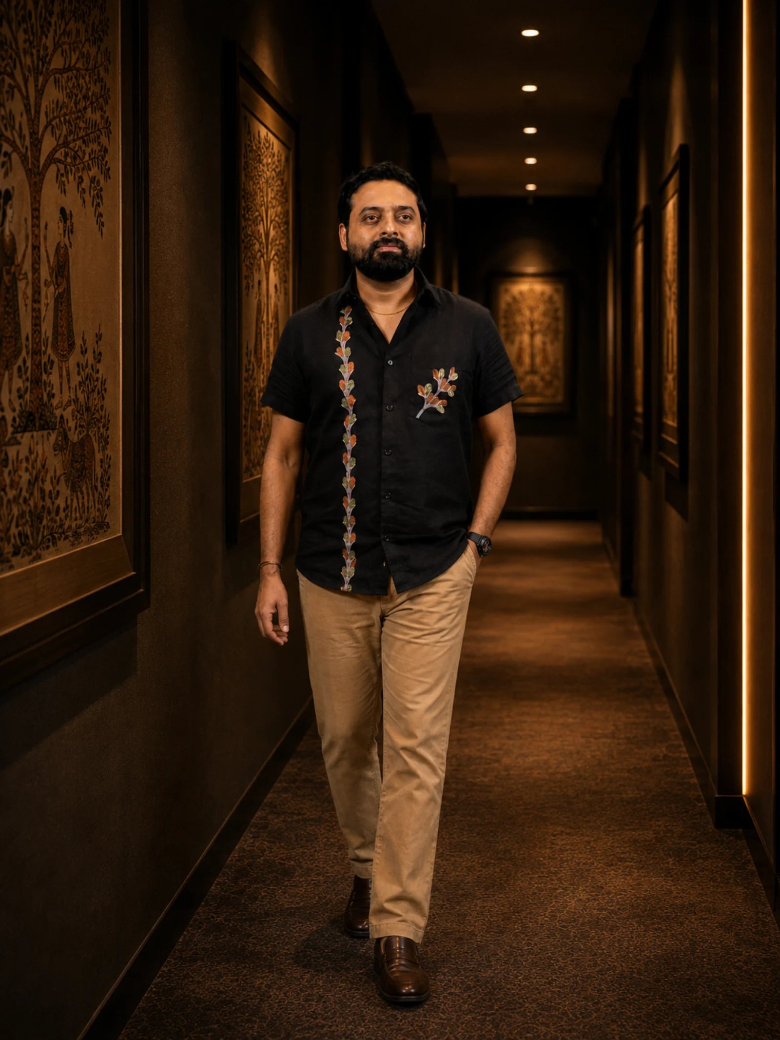 Gond hand-painted linen shirt featuring branching botanical forms along the front placket and chest pocket, observed in an archival corridor setting with softly blurred folk art panels and warm presentation lighting.