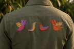 Close-up back view of a Gond hand-painted linen shirt featuring four bird forms arranged horizontally across the back, constructed through layered linear brush detailing with the rear artwork placement fully visible on the linen surface.