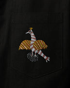 Close-up of a linen shirt pocket featuring a hand-painted Gond bird motif, revealing patterned linear detailing, pigment variation, pocket construction, and visible textile weave.