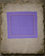Biligiri Kasuti hand-embroidered khadi cotton handkerchief displayed flat on a weathered stone slab, with a repeating Betel Box border worked in yellow and deep plum thread.