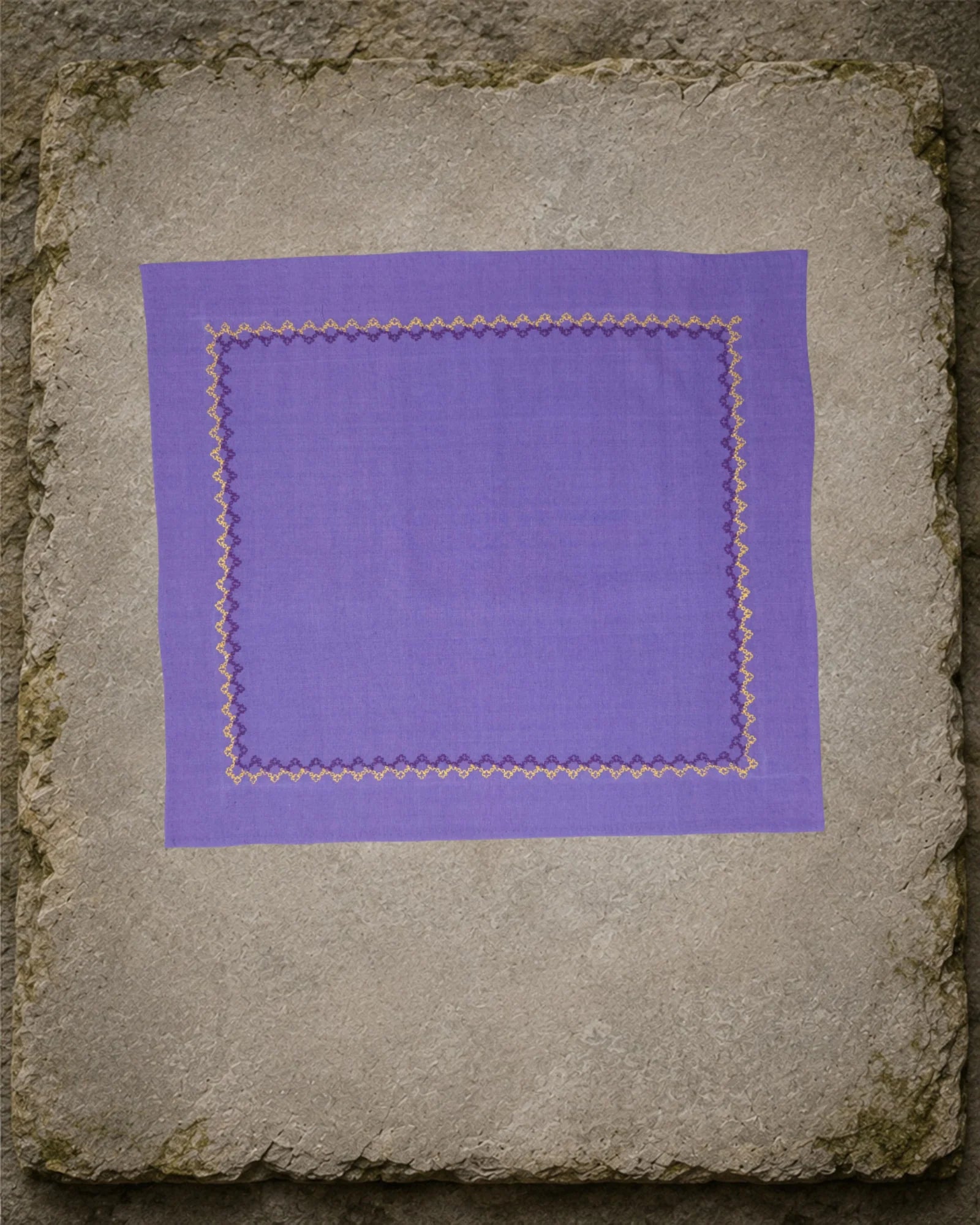 Biligiri Kasuti hand-embroidered khadi cotton handkerchief displayed flat on a weathered stone slab, with a repeating Betel Box border worked in yellow and deep plum thread.