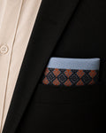 Arka Kasuti pocket square in 100% Mulmul Khadi featuring a Swastik motif rendered through counted hand embroidery in deep indigo and ember-toned threadwork. Styled within the breast pocket of a black tailored jacket, the image draws attention to the disciplined border geometry of Kasuti embroidery, the softened grain of handwoven Mulmul Khadi, and a restrained ceremonial character shaped through quiet archival composition and low, directional lighting.