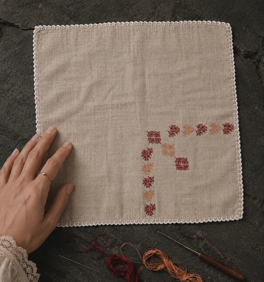 Photographed on a dark stone textile surface beside embroidery threads, crochet needles, and traces of active hand process, this Kasuti pocket square featuring a peacock motif preserves the quiet irregularities of prolonged hand execution. The open Mulmul Khadi surface, counted embroidery intervals, and hand-crocheted edging reveal the layered cadence characteristic of Karnataka’s Kasuti tradition.