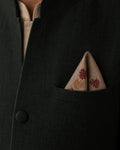 Dhvani hand embroidered Kasuti pocket square in 100% Mulmul Khadi featuring peacock and interconnected geometric motifs rendered in garnet red and burnished copper threadwork. Folded within the pocket of a deep forest-toned Nehru jacket, the composition brings together ceremonial Indian tailoring and the tonal rhythm of counted Kasuti embroidery, while the softened khadi weave and restrained archival lighting preserve a tactile sense of depth and enduring handcrafted character.