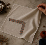 Load image into Gallery viewer, Finished with hand-crocheted edging, this Kasuti pocket square featuring a Swastik motif preserves subtle weave irregularities and softened surface variations formed through prolonged hand execution. Photographed within a slow craft environment shaped by textile practice and material continuity, Ritam reflects an approach to ornamentation rooted in geometry, repetition, and disciplined hand embroidery traditions of Karnataka.