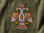 Close-up of hand-painted Odisha Pattachitra detailing on a linen shirt pocket showing intertwined bird forms, lotus elements, and fine painted linework.