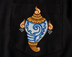 Close-up of hand-painted Odisha Pattachitra detailing on a linen shirt pocket showing a conch form, ornamental borders, and fine painted linework.