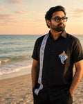 Odisha Pattachitra hand-painted linen shirt featuring a conch artwork on the chest pocket and vertical detailing composed of floral and conch forms along the placket, observed along the seashore in warm sunset light.