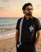 Odisha Pattachitra hand-painted linen shirt featuring a conch artwork on the chest pocket and vertical detailing composed of floral and conch forms along the placket, observed along the seashore in warm sunset light.