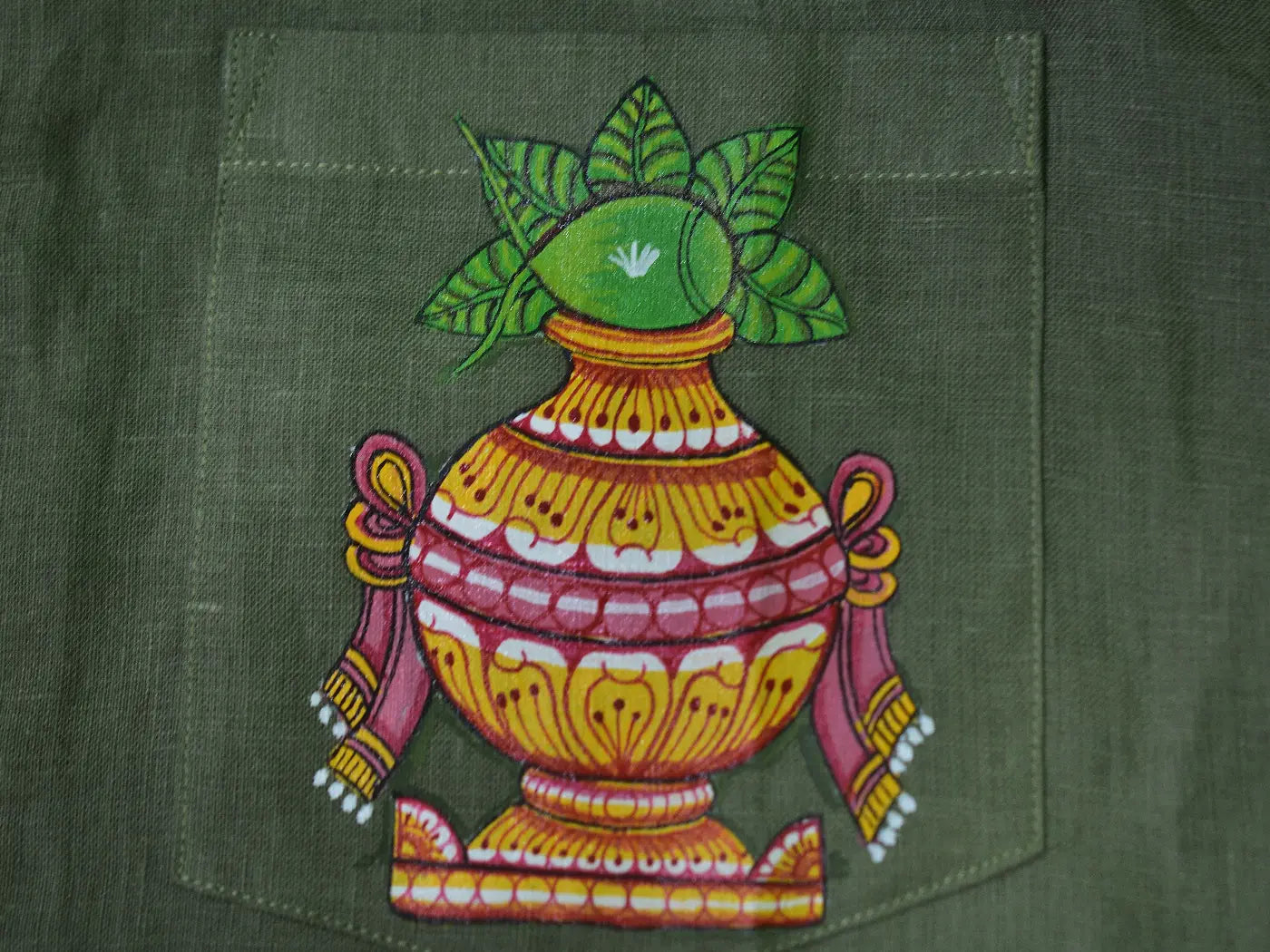 Close-up of hand-painted Odisha Pattachitra detailing on a linen shirt pocket showing a ceremonial kalash form with mango leaves, ornamental borders, and fine painted linework.