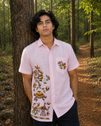 Sohrai Aikya hand-painted linen shirt in a forest setting, showing the peacock, peahen, monkey, turtle, birds and vegetation across the right front panel, with bird and vegetation artwork on the left chest pocket.