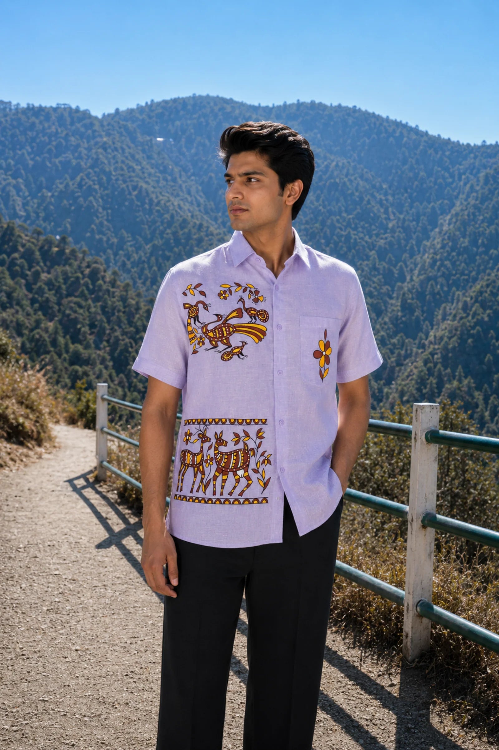 Sohrai Jar hand-painted linen shirt in a mountain setting, featuring peacock and peahen and foliage on the right chest, bordered stag and doe surrounded by flowers and leafy branches within painted horizontal borders below and a flower on the pocket.